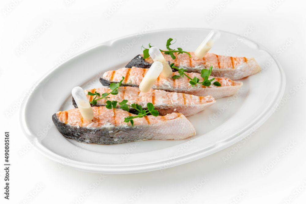 Grilled salmon fillet with sauce on a white plate. Banquet festive dishes. Gourmet restaurant menu. White background. Grilled salmon fillet with sauce on a white plate. Banquet festive dishes. Gourmet restaurant menu. White background.