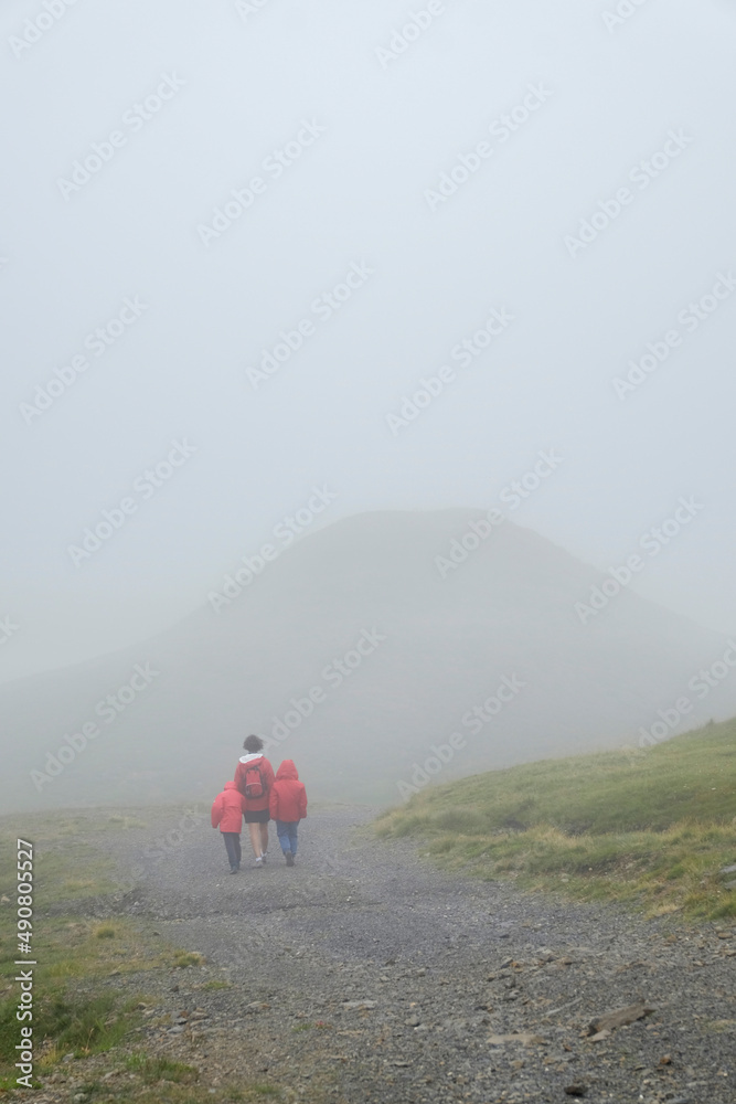 a young mother with her two children holding hands strolls through a mountain landscape on a foggy day