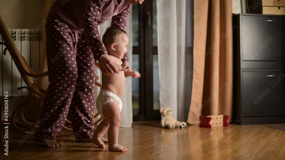 The baby learns to walk with the help of his mother. Young woman leads the child by the handle, helping to start walking, slow motion