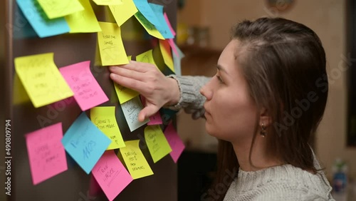A young woman walks up to the refrigerator door, finds the note she needs, and stick on door this sticker.