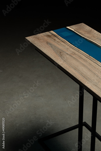 Expensive vintage furniture. The table is covered with epoxy resin and varnished. Luxury quality wood processing. Wooden table on a dark background. A blue epoxy river in a round tree slab.