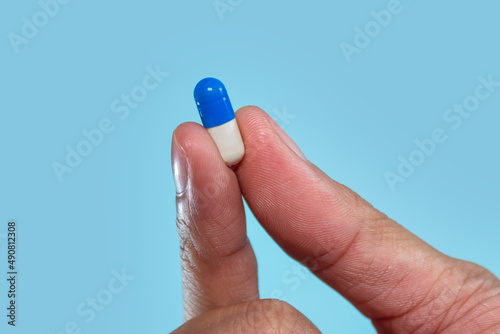 Dedos sosteniendo capsula sobre fondo azul.