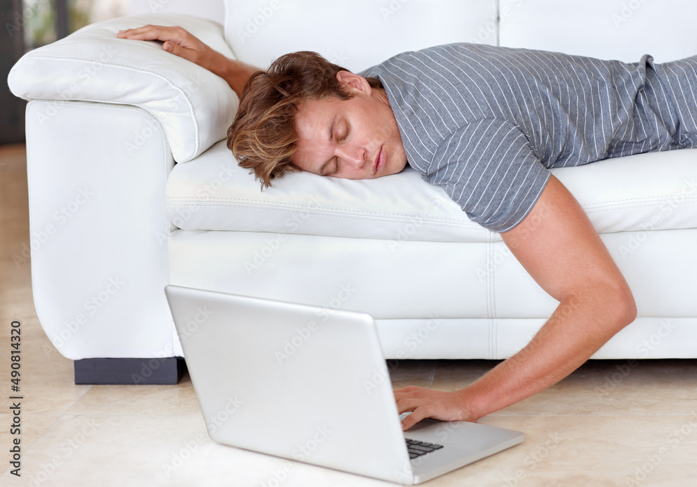 High-speed connection for couch potatoes. A young man lying on his couch with his hand resting on his laptops keyboard. High-speed connection for couch potatoes. A young man lying on his couch with his hand resting on his laptops keyboard.
