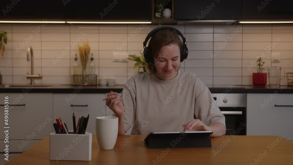 Happy girl in headphones works on a tablet in the living room and listens to music Happy girl in headphones works on a tablet in the living room and listens to music