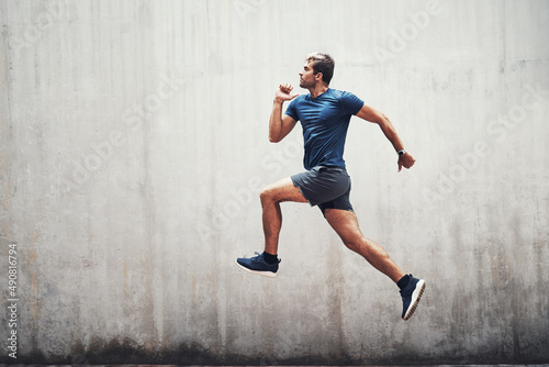 Keep up the energy. Shot of a sporty young man running against a grey wall outdoors.