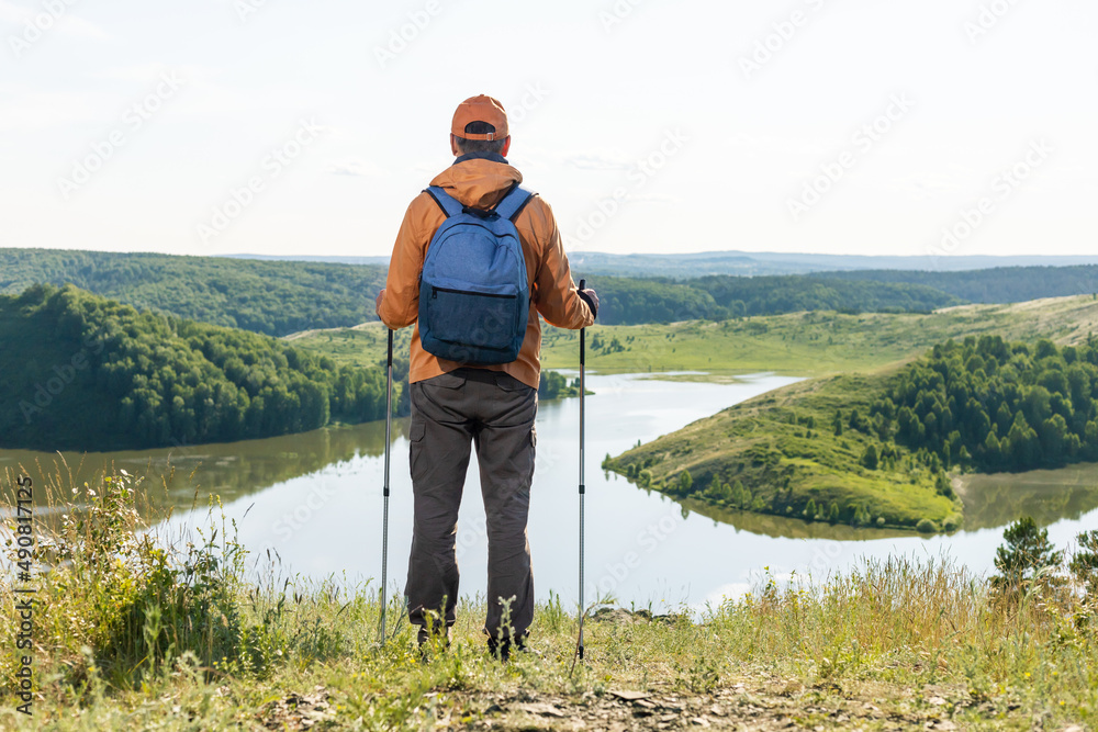 Man solo traveling backpacker hiking in  mountains. Tourist stands near lake enjoying the sunset, thinking.