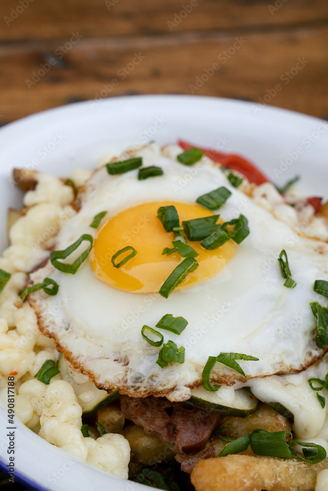 Closeup view of fried potatoes with melted cheese, chorizo, bell pepper, onion and a grilled egg in a white dish.