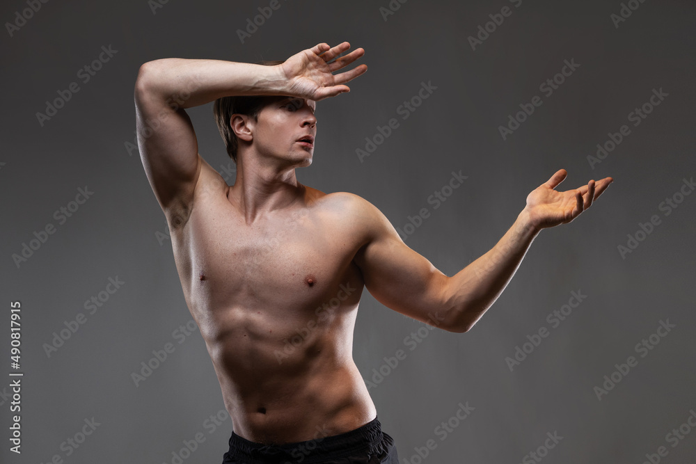 Obraz premium A young muscular man in an expressive pose. Beautiful muscles. extraordinary athletic body. Portrait on a gray background