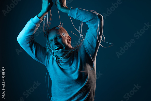 A young man with his head entangled in wires is trying to pull out electrical contacts from his head, signals to the brain. Neurointerface, future technologies, creative concept. © Ulia Koltyrina