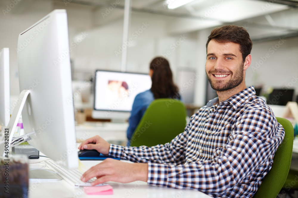 Im working on something big. Portrait of a handsome young designer sitting at his desk with a colleague in the background. Im working on something big. Portrait of a handsome young designer sitting at his desk with a colleague in the background.
