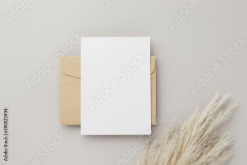 Blank greeting card invitation Mockup 5x7 on Brown envelope with dried flowers on beige background, flat lay, mockup