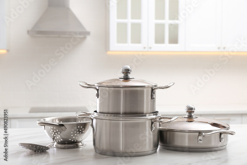 Set of stainless steel cookware and kitchen utensils on white table indoors