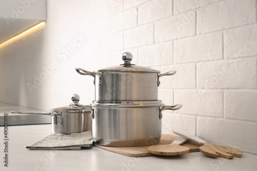 Set of stainless steel cookware and kitchen utensils on table near white brick wall