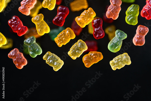 Multicolored flying gummy bears on a black background, flat lay