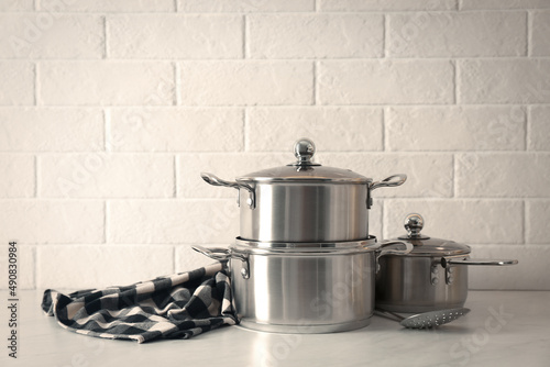 Set of stainless steel cookware on table near white brick wall