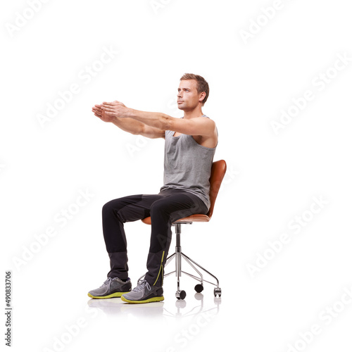 Keeping his limbs long and lean. A handsome young man wearing gym clothes and stretching while seated in an office chair against a white background.