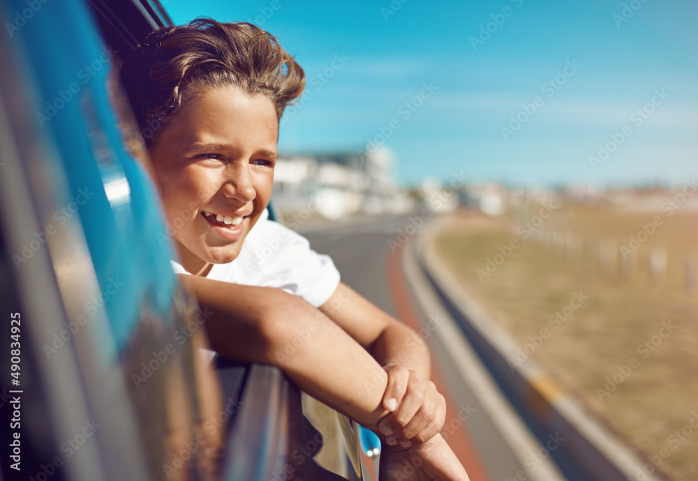 Fototapeta premium Are we there yet. Shot of a happy young boy leaning out of the car window on a trip to the beach.