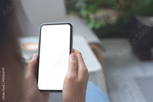 Cell phone mockup image blank white screen.  Woman hand holding, using mobile phone at coffee shop.