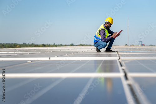 African man engineer using digital tablet maintaining solar cell panels on building rooftop. Technician working outdoor on ecological solar farm construction. Renewable clean energy technology concept