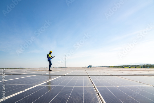 African man engineer using digital tablet maintaining solar cell panels on building rooftop. Technician working outdoor on ecological solar farm construction. Renewable clean energy technology concept