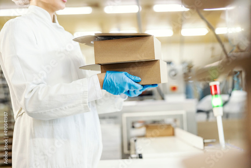Cropped picture of female food factory worker's hands carry boxes with baking products.