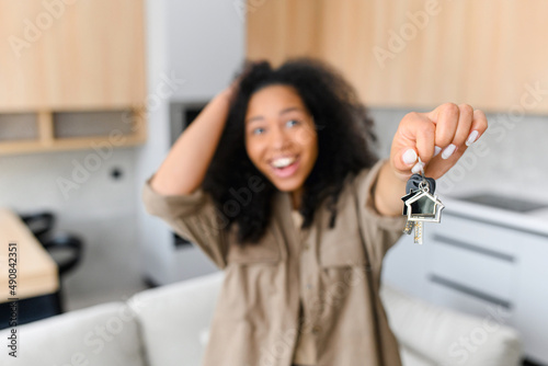 Obraz na plátně Joyful multiracial woman holding keys with trinket in shape of little cute house