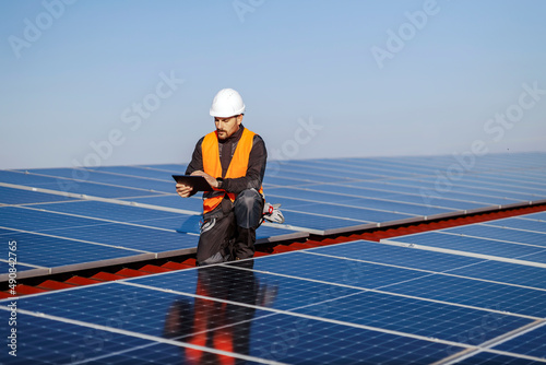 A supervisor kneeling and checking on correctness of solar panels on the roof.