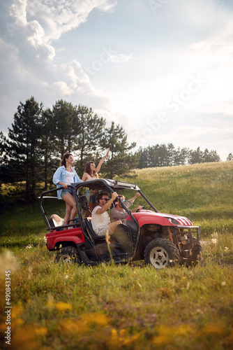 Young happy friends enjoying beautiful sunny day while driving a off road buggy car on mountain nature. Freedom, friendship, nature concept.