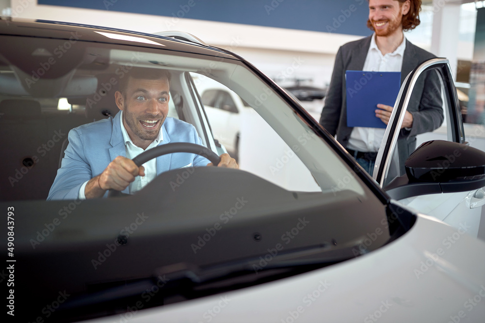 A customer in the auto shop is very excited while testing a new car attend to buy. Car, shop, buying