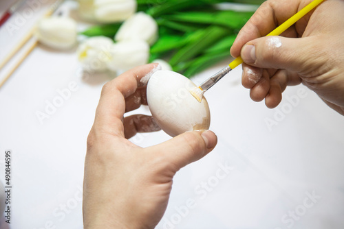 A man's hand paints an Easter egg with a yellow brush close-up. The concept of the holiday and Easter decor