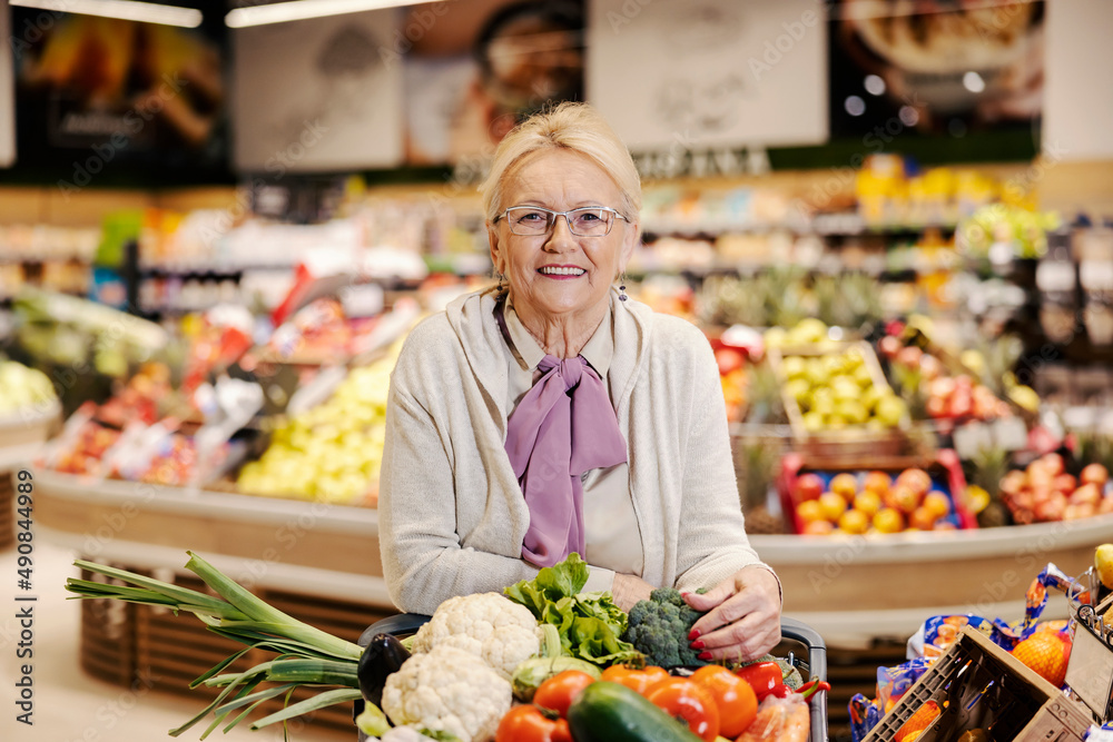 Senior woman purchasing organic vegetables at supermarket and smiling at the camera.