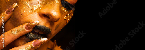 Beauty fashion model girl with golden make-up and body on black background. Golden body art. The golden face of a beautiful lady is touching. Artistic portrait.