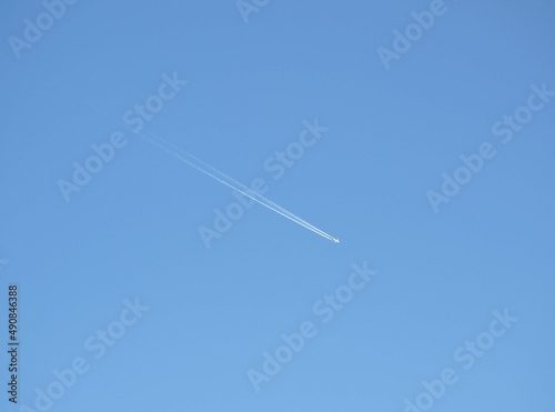 A flying plane leaving a white trail against a blue sky.