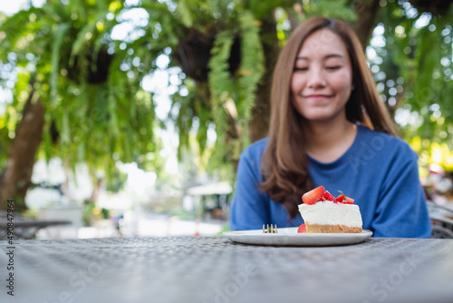 Blurred image of a young woman looking at a piece of strawberry cheese cake on the table