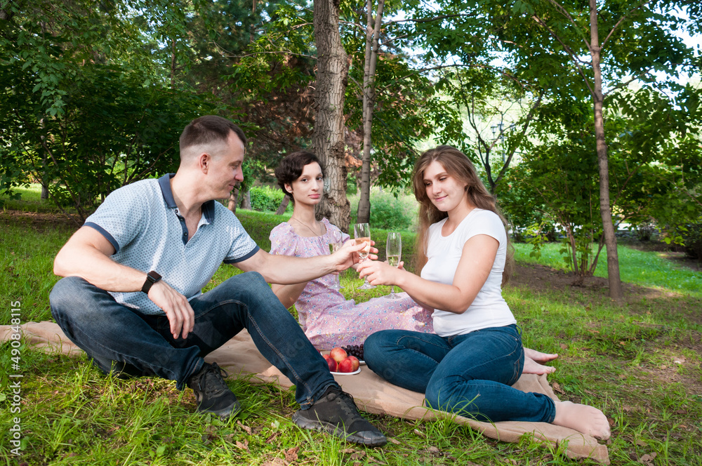 A man treats two girls to wine at a summer picnic in the park