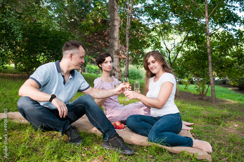 A man treats two girls to wine at a summer picnic in the park