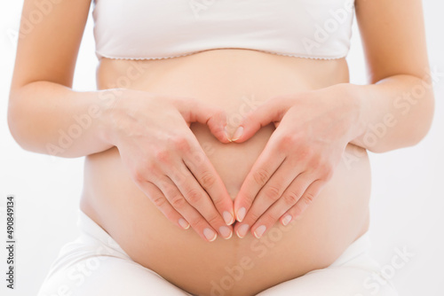 Wallpaper Mural Heart shape created from young adult pregnant woman hands on big naked belly on white background. Pregnancy time. Baby expectation. Love, happiness and safety concept. Closeup. Front view. Torontodigital.ca
