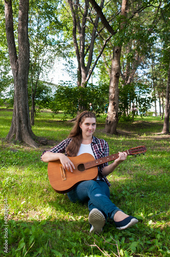 Beautiful girl playing guitar on the lawn in the park