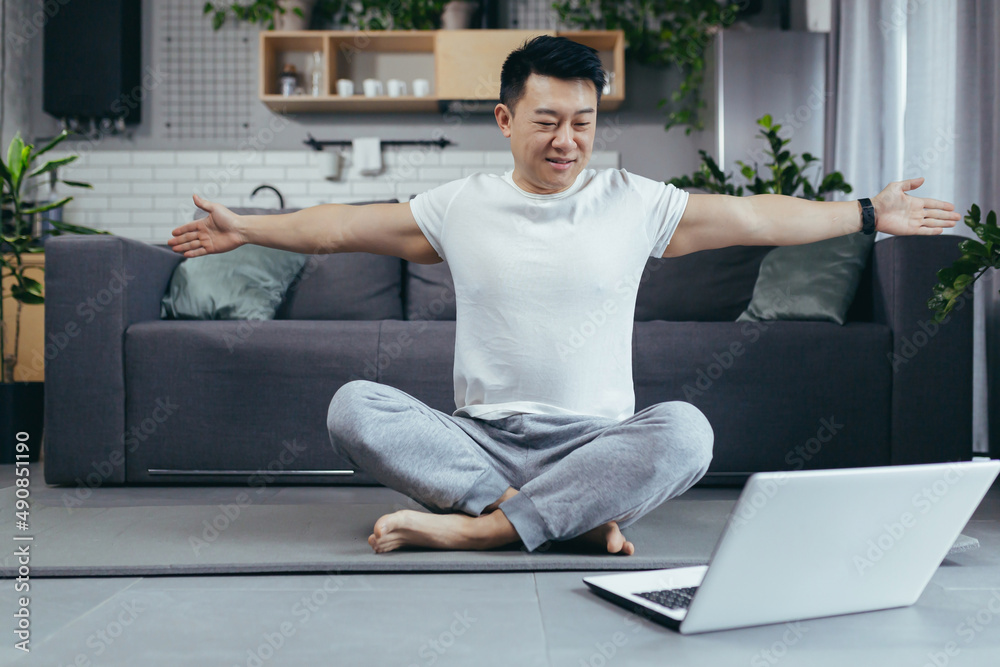 Asian man at home, engaged in fitness online, uses laptop for joint activities, active lifestyle
