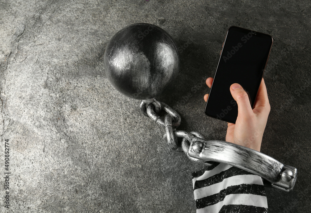 Prisoner shackled with ball and chain holding smartphone at grey table, top  view Photos | Adobe Stock