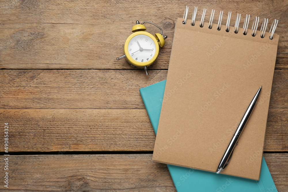 Notebooks, pen and alarm clock on wooden table, flat lay. Space for text Notebooks, pen and alarm clock on wooden table, flat lay. Space for text
