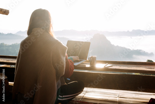 Young business woman working at the computer in cafe on the rock. Young girl downshifter working at a laptop at sunset or sunrise on the top of the mountain to the sea, working day.. photo