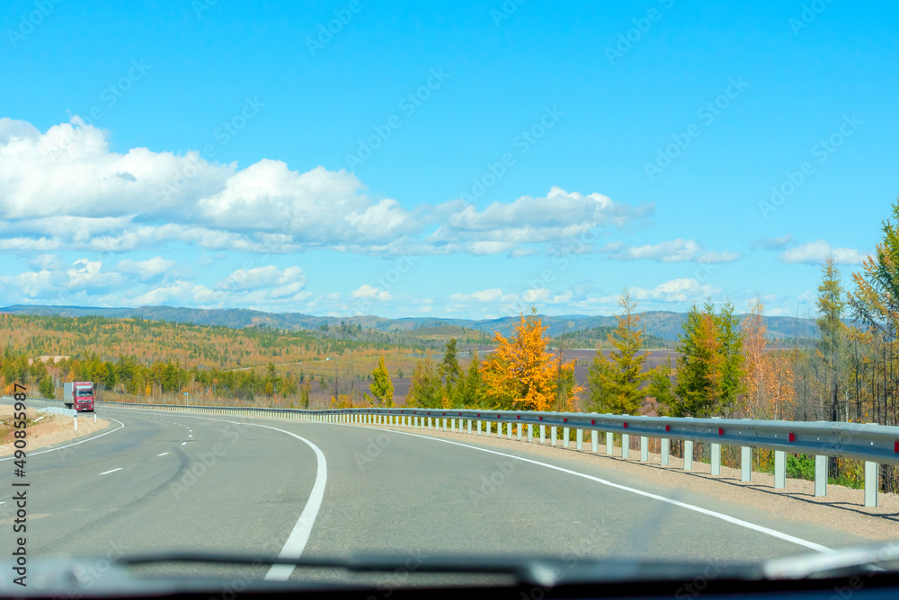 Fototapeta premium Bright autumn scene with road among orange and green trees and blue sky. Soft selective focus. Beauty of nature, travel concept