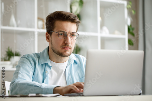 An attractive young man is working on a laptop.