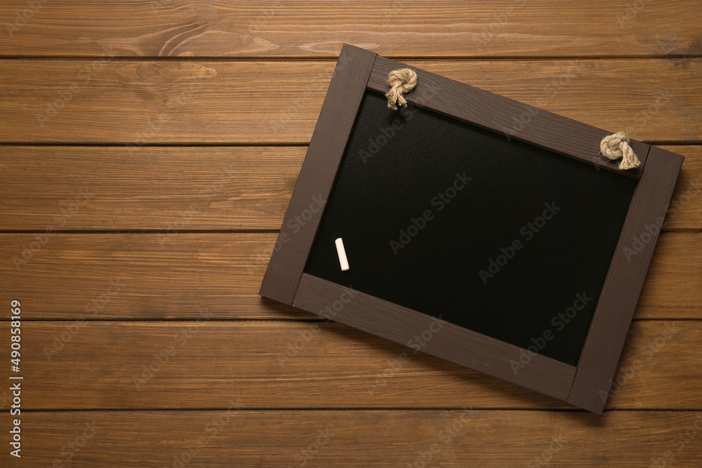Obraz premium Clean small blackboard with piece of white chalk on wooden table, top view. Space for text