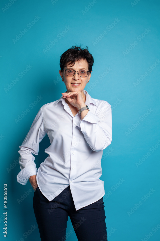 Good looking beautiful smart positive mature female smiling at camera on blue background Good looking beautiful smart positive mature female smiling at camera on blue background