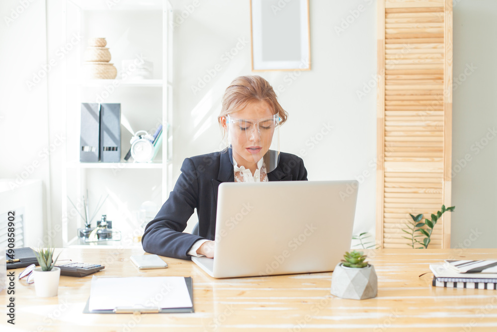 Portrait of business woman in protective face shield using laptop in office Portrait of business woman in protective face shield using laptop in office