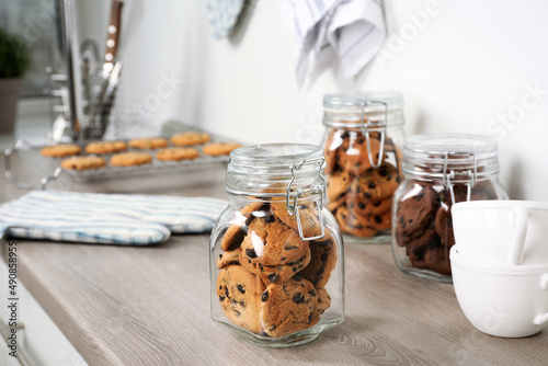Fotografiet Delicious chocolate chip cookies in glass jars on wooden table in kitchen