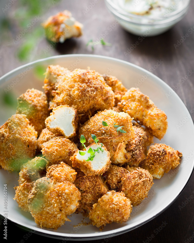crispy breaded cauliflower with herbs and sauce in a white plate on a brown background vertical photo crispy breaded cauliflower with herbs and sauce in a white plate on a brown background vertical photo