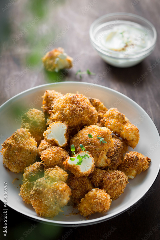 crispy breaded cauliflower with herbs and sauce in a white plate on a brown background vertical photo crispy breaded cauliflower with herbs and sauce in a white plate on a brown background vertical photo